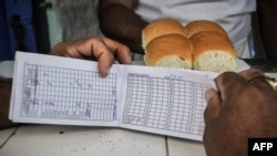 Una cubana muestra su vieja libreta de racionamiento junto a una ración de pan. (AFP/Archivo)