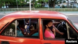 Cubanos viajan en auto usando mascarilla facial. (REUTERS/Alexandre Meneghini)