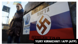 Una joven pasando junto a un cartel con una esvástica nazi en la bandera rusa y las palabras "Colores de los ocupantes". Kyiv, Ucrania, 12 de marzo de 2014. Foto: Yury Kirnichny (AFP)