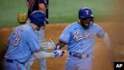 El cubano Adolis García (derecha) celebra junto a Jonah Heim (izquierda) luego de anotar la carrera de la ventaja en la octava entrada del juego ante los Guardianes de Cleveland, en Arlington, Texas. Domingo 16 de julio de 2023. (AP Foto/Gareth Patterson).