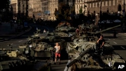 Varias personas caminan entre vehículos militares rusos destruidos instalados en el centro de Kiev, Ucrania, el 24 de agosto de 2022. (AP Foto/Evgeniy Maloletka)