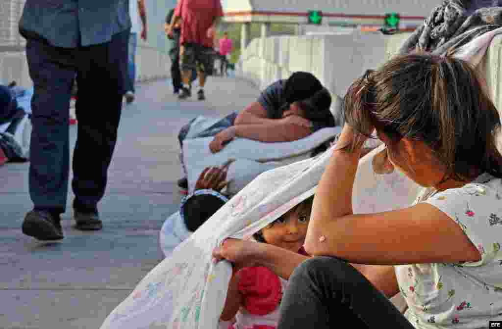 Jennifer, de 2 años, y su madre Evelyn (dcha) aguardan en un puente cerca de la frontera entre EE. UU. y México junto a otros solicitantes de asilo de Guatemala y Cuba en espera de poder entrar EE.UU. en Matamoros (México) el 29 de junio de 2018.