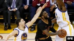 Kyrie Irving (c) trata de convertir una cesta ante la marca de Klay Thompson (i) y Festus Ezeli (d), de Warriors.