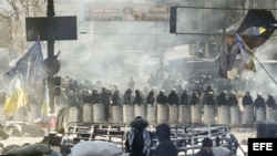 Varios manifestantes permanecen tras una barricada ante un cordón policial en Kiev (Ucrania) el viernes 31 de enero de 2014.