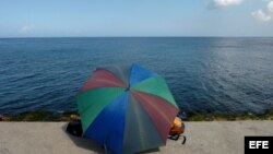 Una pareja conversa bajo una sombrilla en el malecón habanero en el día de San Valentín.