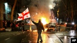 Un hombre agita una bandera de Georgia frente a una barricada en llamas cerca del parlamento en Tiflis, Georgia, el 9 de marzo de 2023. (AP Foto/Zurab Tsertsvadze)