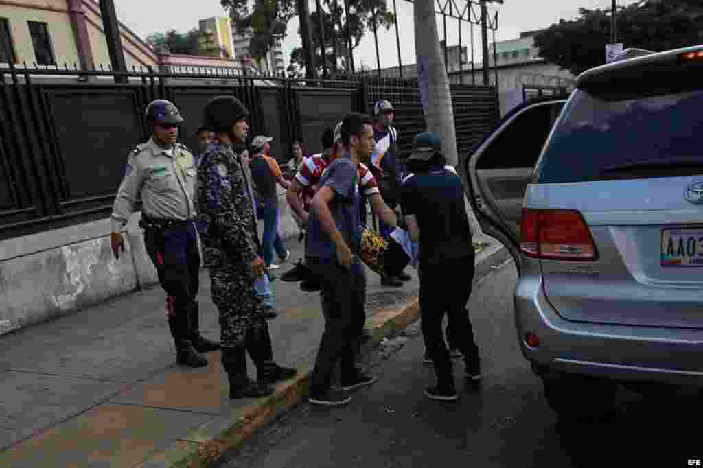 Dos hombres introducen a una persona herida en un coche durante un enfrentamiento entre un grupo de personas adeptas al oficialismo y personas opositoras.