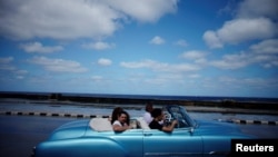 Turistas pasean por el Malecón de La Habana en un auto clásico americano. 