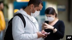 Pasajeros usando mascarillas como precaución contra el contagio del nuevo coronavirus usan sus teléfonos en el Aeropuerto Internacional de Sao Paulo, Brasil.