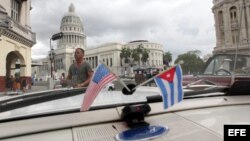 El capitolio cubano desde el interior de un auto clásico con las baderas de EEUU y Cuba.