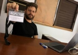 El artista cubano Leandro Feal sostiene una tarjeta de presentación que dice: "inspector", un performance que denuncia la figura de control artístico amparada bajo el Decreto Ley 349.