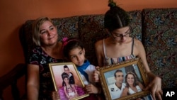 Danmara Triana (izquierda), con sus hijas Alice (centro) y Claudia, muestran fotos suyas con su hermano y su padre, quienes emigraron a Estados Unidos en 2015. (AP Foto/Ramón Espinosa)