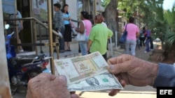 Un hombre muestra un peso convertible cubano y un dólar estadounidense frente a una oficina de la Western Union en La Habana.