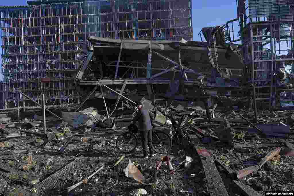 Un hombre parado con su bicicleta en medio de la destrucción causada por el bombardeo ruso en un centro comercial en Kyiv, Ucrania. Foto: AP/Rodrigo Abd.