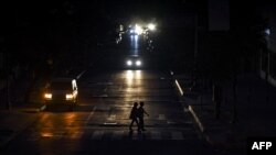 Transeúntes cruzan a oscuras el lunes una calle de Caracas, iluminados solamente por los focos de un vehículo (Foto: AFP).