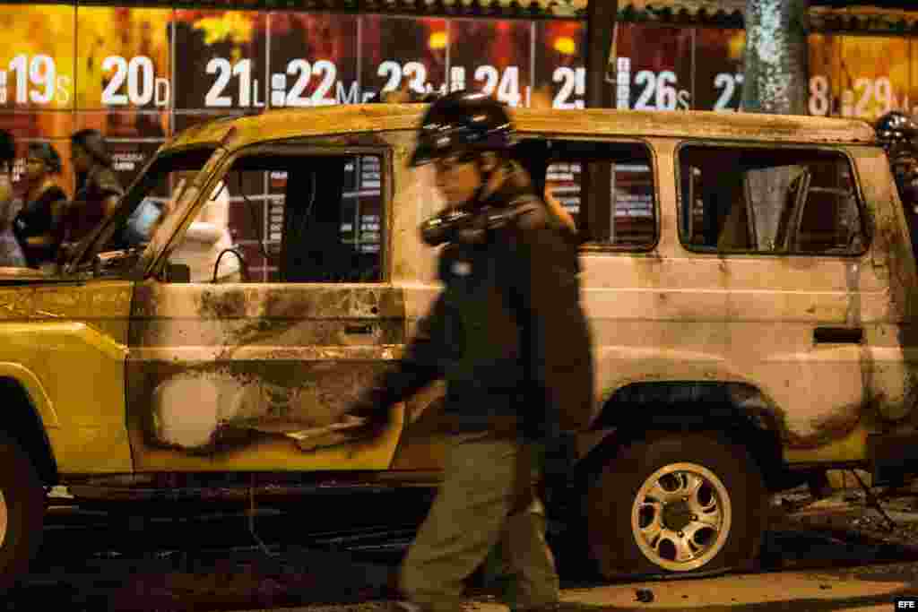 Un integrante de la Guardia Nacional Bolivariana (GNB) camina frente a una camioneta del mismo cuerpo de seguridad, que fue incendiada por manifestantes opositores al gobierno nacional .