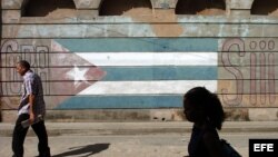 Varias personas caminan junto a una bandera pintada sobre un muro.