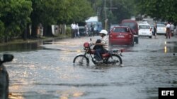 Un hombre conduce una motocicleta por una calle inundada en La Habana. (EFE/Archivo)