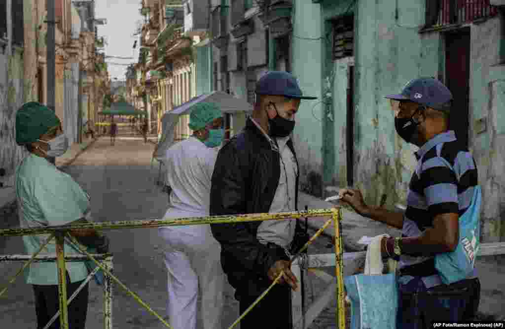 Un residente muestra su identificación a un oficial de policía que está limitando el acceso a un vecindario como una forma de frenar la propagación de la pandemia de COVID-19,&nbsp; 22 de febrero de 2021. (AP Foto/Ramon Espinosa)